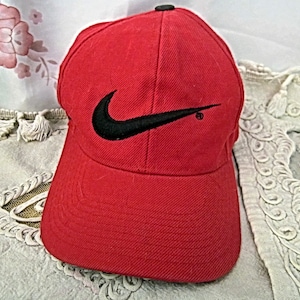 Könnte beinhalten: Eine rote Baseballkappe mit einem schwarzen Nike-Swoosh-Logo.