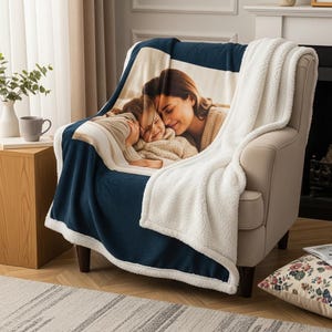 May include: A cozy navy blue and white blanket draped over a beige armchair. The blanket features a printed photograph of a mother and child. The blanket has a white sherpa lining and a navy blue border.