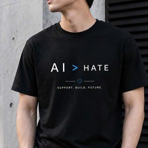May include: Black t-shirt with the text "AI > HATE" in white and blue. The shirt also has the text "SUPPORT. BUILD. FUTURE." below the main text. The shirt is a crew neck style.
