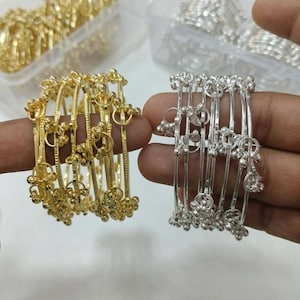 May include: Gold and silver bangles with floral and circular designs. The gold bangles are on the left, and the silver bangles are on the right. Both sets of bangles are held by a person's fingers.