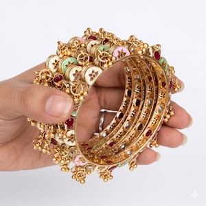 May include: A set of gold-toned bangles featuring dangling charms with enamel accents in shades of pink, green, and white. The circular bracelets are embellished with small red stones and intricate metalwork, creating a layered, ornate appearance.
