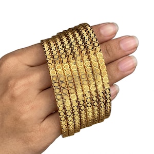 Può includere: Un set di sei bracciali rigidi color oro caratterizzati da un motivo circolare ripetuto con linee orizzontali testurizzate all'interno di ogni cerchio. I bracciali presentano una finitura metallica lucida e una larghezza costante.