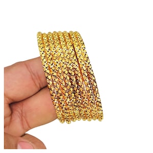 May include: A set of six gold-colored bangles featuring a repeating diamond-shaped cross-hatch texture across the entire surface of each circular band. The bangles are arranged in a parallel stack, showcasing a bright, reflective metallic finish.