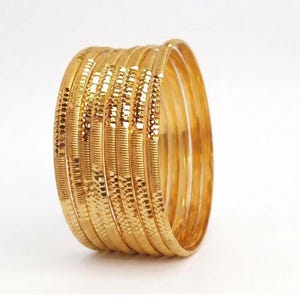 May include: A collection of gold bangles with textured surfaces. The bangles have a shiny, reflective finish and are arranged in a semi-circular shape against a white background. The bangles are a warm, golden colour.