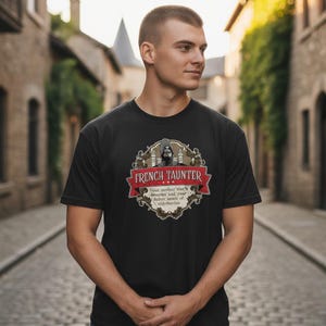May include: Black t-shirt with a graphic design. The design features the text "FRENCH TAUNTER" in red on a banner, an illustration of a hooded figure, and the text: "Your mother was a hamster and your father smelt of elderberries."