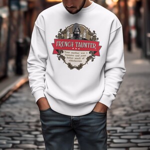 May include: White sweatshirt featuring a graphic with the text "FRENCH TAUNTER" in red. The design includes a medieval illustration and the quote "Your mother was a hamster and your father smelt of elderberries."