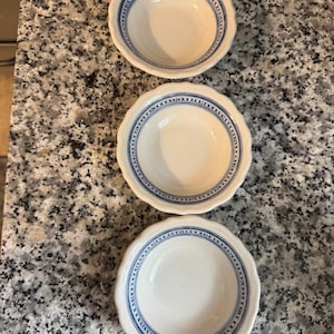 May include: Three small, white ceramic bowls with a scalloped edge and a blue patterned border. The bowls are arranged in a vertical line, each with a slightly different perspective.