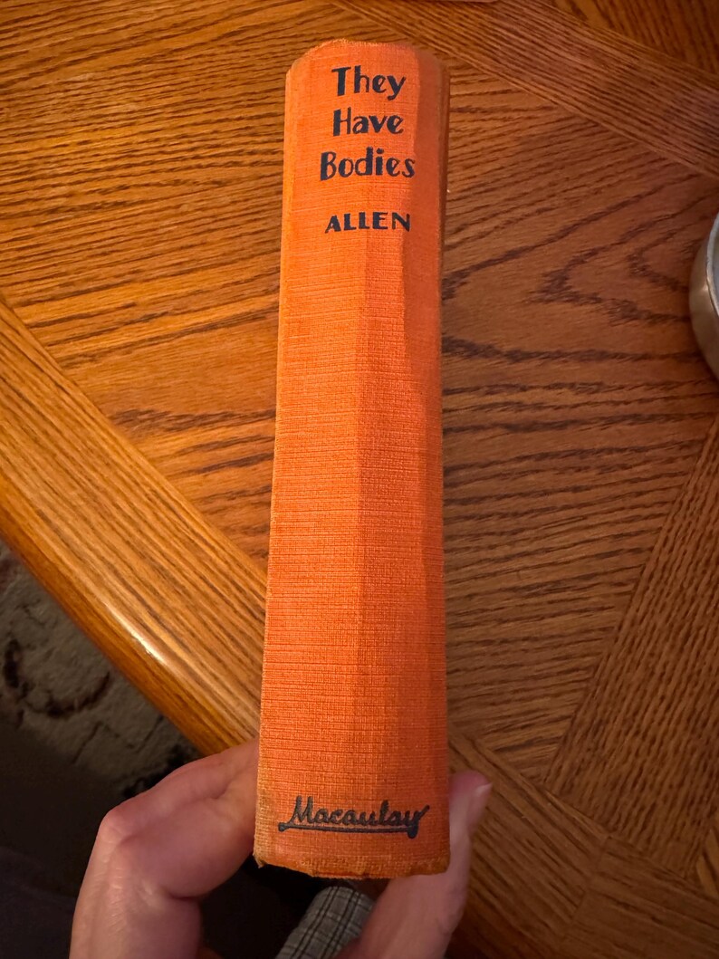 K&ouml;nnte beinhalten: Ein Vintage-Buch mit dem Titel "They Have Bodies" von Allen. Das Buch hat einen orangefarbenen Einband mit dem Titel und dem Namen des Autors in Schwarz. Der Name des Verlags, Macaulay, ist unten aufgedruckt. Das Buch wird vertikal gehalten.