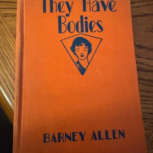 K&ouml;nnte beinhalten: Ein orangefarbenes Hardcover-Buch mit dem Titel "They Have Bodies" und dem Namen des Autors, Barney Allen, in dunkelblauer Schrift. Eine dreieckige Grafik mit einem Frauengesicht befindet sich auf dem Cover.