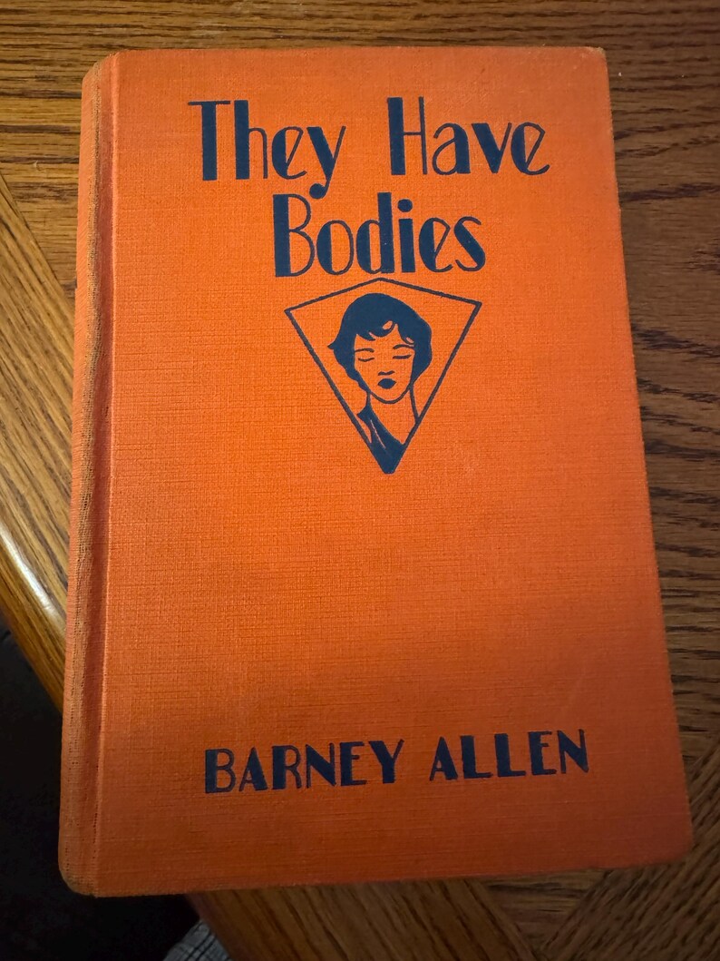 K&ouml;nnte beinhalten: Ein orangefarbenes Hardcover-Buch mit dem Titel "They Have Bodies" und dem Namen des Autors, Barney Allen, in dunkelblauer Schrift. Eine dreieckige Grafik mit einem Frauengesicht befindet sich auf dem Cover.