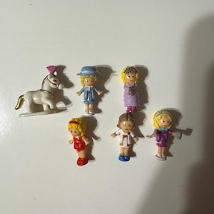 May include: A collection of miniature plastic figures and a white horse toy. The figures include a girl in a red outfit, a girl in a blue suit and hat, a girl in a purple dress, and a girl in a white coat.