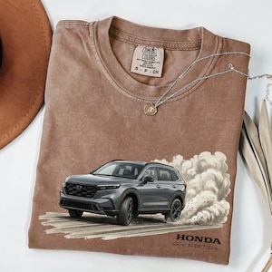 May include: A brown Comfort Colors t-shirt featuring a gray Honda CR-V Sport SUV graphic with a cloud of smoke. The text "HONDA CR-V SPORT SUV" is printed below the car. A silver necklace with a pendant is draped across the shirt.
