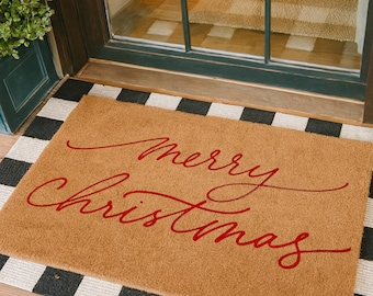 Puede incluir: Una alfombra rectangular con las palabras "Merry Christmas" en escritura roja. La alfombra es de color beige con un borde a cuadros blanco y negro, colocada frente a una puerta con ventana de vidrio.