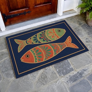 Puede incluir: Una alfombra rectangular con fondo azul marino y borde decorativo. Dos peces estilizados en naranja, verde y beige están centrados en la alfombra. La alfombra está colocada frente a una puerta de madera.