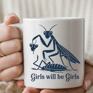 May include: White ceramic mug featuring a dark blue illustration of praying mantises and a cockroach. The mug has the text "Girls will be Girls" in a stylized font. The mug is held by a person.