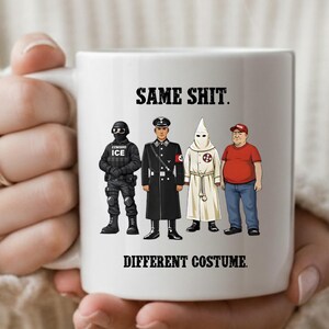 May include: White ceramic mug featuring the text "SAME SHIT. DIFFERENT COSTUME." The mug displays illustrations of four figures in different uniforms and attire. The mug is held by a person.