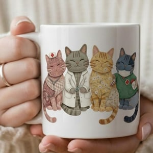 Puede incluir: Taza de cerámica blanca con un diseño de cuatro gatos de dibujos animados con atuendos médicos. Los gatos están representados como enfermera, médico y médico, con uno que lleva una mascarilla. La taza está sostenida por una persona.