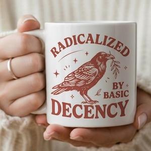 May include: A white ceramic mug with a black handle and the text "But First, Coffee" in a black, bold font. The mug is on a white surface.