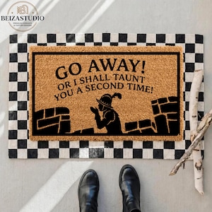 Può includere: Un zerbino rettangolare con un bordo a scacchi bianco e nero. Il centro presenta una superficie in fibra di cocco marrone con il testo "GO AWAY! OR I SHALL TAUNT YOU A SECOND TIME!" e una silhouette di una figura medievale.