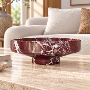 Puede incluir: Un cuenco de mármol rojo intenso con vetas blancas prominentes. El cuenco presenta una base circular robusta y un recipiente ancho y poco profundo, destacando la textura natural de la piedra pulida y los patrones del material rojo.