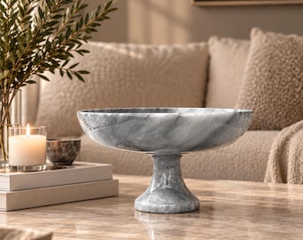 Puede incluir: Un cuenco de pedestal de mármol gris y blanco con un recipiente ancho y poco profundo y una base robusta y acampanada. El cuenco presenta patrones de vetas de piedra natural en toda su superficie pulida, creando un aspecto continuo.