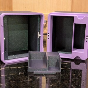 Puede incluir: Dos cajas de almacenamiento negras y moradas abiertas, con una peque&ntilde;a bandeja dividida. Las cajas tienen forma rectangular con un marco morado y un interior negro. La bandeja es negra y tiene dos compartimentos.