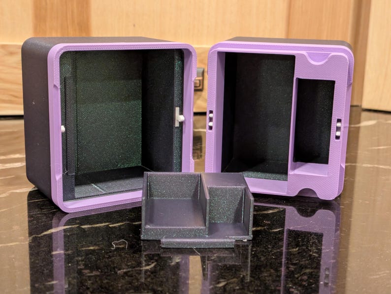 Puede incluir: Dos cajas de almacenamiento negras y moradas abiertas, con una peque&ntilde;a bandeja dividida. Las cajas tienen forma rectangular con un marco morado y un interior negro. La bandeja es negra y tiene dos compartimentos.