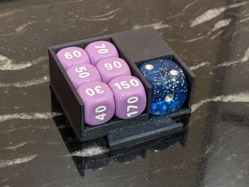 Puede incluir: Un soporte para dados negro impreso en 3D que contiene seis dados lavanda con n&uacute;meros blancos y un dado azul y blanco moteado. Los dados est&aacute;n dispuestos en dos compartimentos, sobre una superficie oscura y brillante.