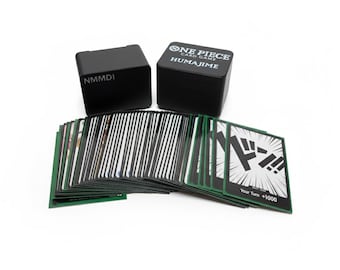 May include: A set of One Piece card game cards with two black storage boxes. The cards have green borders and various illustrations. One box has "NMMDI" printed on it, and the other has "ONE PIECE CARD GAME HUMAJIME" printed on it.