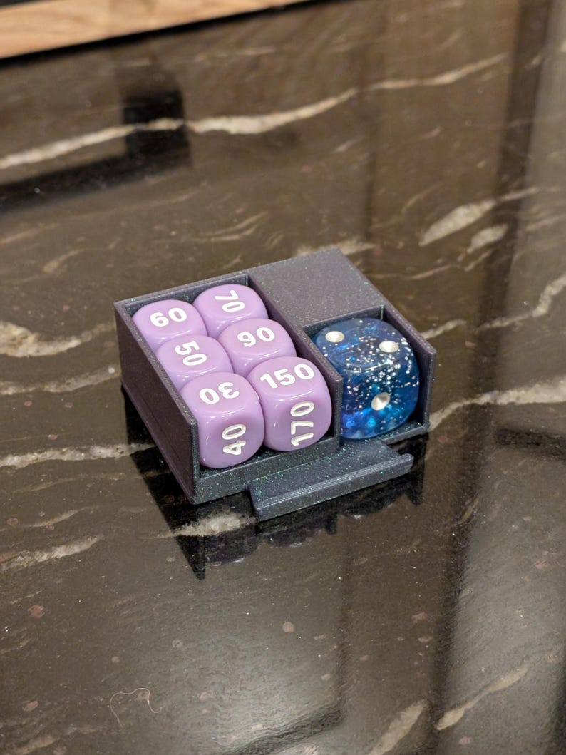 Puede incluir: Un soporte para dados gris oscuro con un compartimento para siete dados morados y un dado azul moteado. Los dados est&aacute;n numerados y el soporte est&aacute; sobre una superficie oscura.