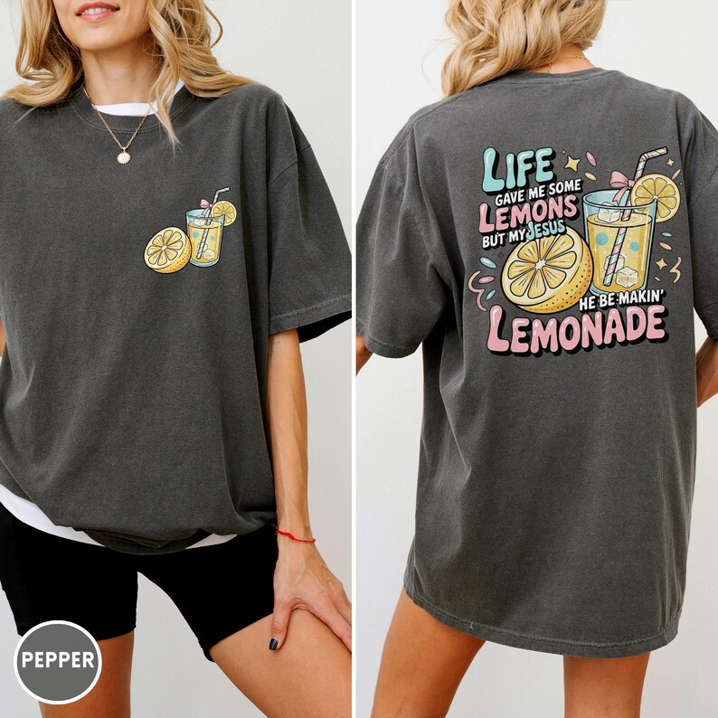 May include: Dark gray t-shirt with a front pocket design of a lemon and a glass of lemonade. The back of the shirt features the text "LIFE GAVE ME SOME LEMONS BUT MY JESUS HE BE MAKIN' LEMONADE" with lemon and lemonade graphics.