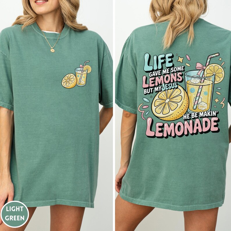 May include: Light green t-shirt with a front pocket graphic of a lemon and a drink. The back of the shirt features the text "LIFE GAVE ME SOME LEMONS BUT MY JESUS HE BE MAKIN' LEMONADE" with a lemon and drink graphic.