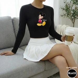Puede incluir: Top negro de manga larga con un estampado de Mickey Mouse, combinado con una falda plisada blanca. La imagen tambi&eacute;n incluye una taza de caf&eacute; y el texto "LONG SLEEVE BLACK".