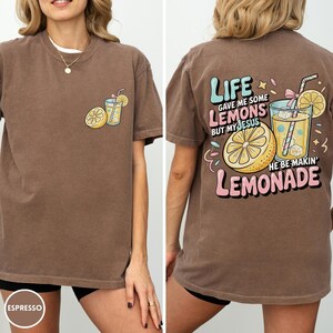 May include: Espresso-colored t-shirt with a graphic of a lemon, a glass of lemonade, and the text "Life gave me some lemons but my Jesus he be makin' lemonade." The shirt has a crew neck and short sleeves.