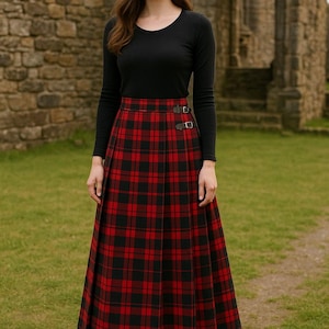 Könnte beinhalten: Ein langer, plissierter rot-schwarz karierter Rock mit zwei dekorativen Schnallen. Der Rock wird mit einem langärmeligen schwarzen Oberteil getragen. Das Outfit wird im Freien vor einem Steingebäude getragen.