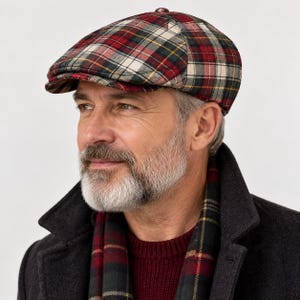 May include: A flat cap featuring a multi-colored plaid pattern in shades of red, dark green, cream, and thin yellow lines. The cap has a rounded crown and a short, stiff brim extending from the front, constructed from a woven fabric material.