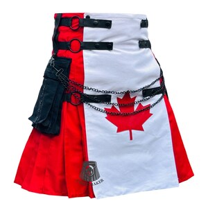 Op de afbeelding: Een kilt met het ontwerp van de Canadese vlag. De kilt heeft een rood-wit kleurenschema met een rood esdoornblad-embleem. Het heeft zwarte riemen, ringen en een ketting. Aan de zijkant zit een zwarte zak.