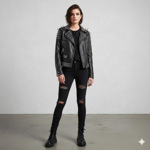 May include: A black leather jacket with silver studs on the shoulders, lapels, and cuffs. The jacket is worn with black jeans with knee rips and black boots. The model is standing in front of a plain white background.