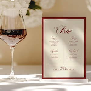 May include: A bar menu with a burgundy border and the text "The Bar" in elegant script. The menu lists wine, beer, spirits, and cocktails. A wine glass filled with red wine is in the foreground, with white flowers in the background.