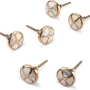 Könnte beinhalten: Sechs dekorative Schrankknöpfe. Jeder Knopf hat eine runde, weiße Perlmuttmitte mit einem goldfarbenen Kreuzdesign. Die Knöpfe haben eine goldfarbene Metallbasis und eine Gewindeschraube zur Befestigung.