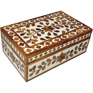 Puede incluir: Caja rectangular de madera con un diseño floral incrustado. La caja presenta un fondo blanco con patrones florales marrones y beige. Los bordes están adornados con madera marrón oscuro. La caja está cerrada.