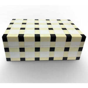 Può includere: Una scatola rettangolare con un motivo a griglia geometrica composto da piastrelle quadrate e rettangolari alternate di colore nero, bianco e crema. La scatola presenta un coperchio piatto e una silhouette strutturata con bordi netti.