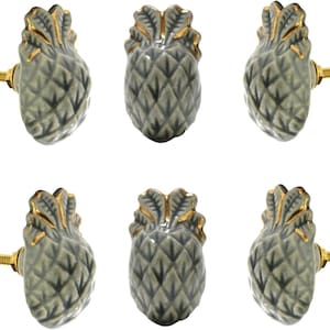 Peut inclure: Six boutons de meuble en céramique en forme d'ananas. Les boutons sont de couleur vert mat avec des accents dorés sur la couronne. Chaque bouton est doté d'une vis dorée pour l'installation. Le design ananas ajoute une touche tropicale aux meubles.