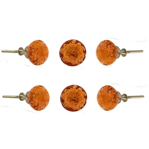 Puede incluir: Un juego de seis pomos redondos para armarios con una superficie de vidrio naranja translúcido con burbujas de aire incrustadas. Cada pomo está unido a un poste y una base de metal plateado, ofreciendo un aspecto uniforme para muebles.