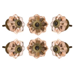 May include: A set of six flower-shaped cabinet knobs made of translucent pale pink glass. Each knob features a fluted petal design with a central antique brass-toned metal rosette and a dark circular screw mount at the very center of the piece.