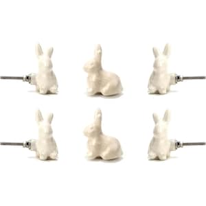 May include: Six off-white ceramic bunny-shaped cabinet knobs. Each knob features a detailed bunny design and a metal screw for attachment. The knobs are arranged against a white background, ideal for adding a touch of whimsy to furniture.