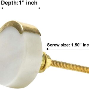 May include: A white cabinet knob with a gold-colored metal accent. The knob has a depth of 1 inch and a screw size of 1.50 inches. The knob is designed for furniture and home decor.