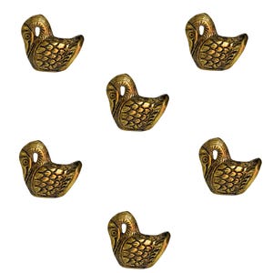 May include: Six identical brass-coloured metal swan figurines arranged in a pattern. Each swan is depicted in a side profile with a curved neck, a small head, and detailed embossed feather patterns covering the body, finished in a metallic gold tone.
