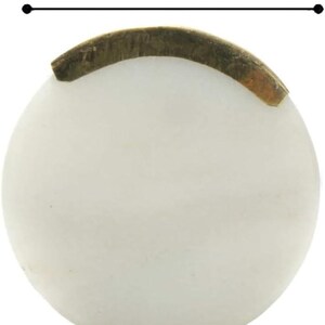 May include: A round, off-white object with a diameter of 1.60 inches. A curved, brass-colored metal piece is affixed to the top. The object appears to be a decorative element or component, possibly for furniture or crafts.