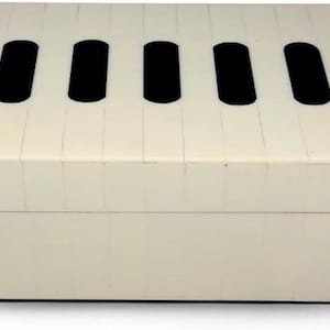 Puede incluir: Una caja de almacenamiento rectangular con una superficie de color crema y un patrón repetitivo de formas ovaladas negras verticales a lo largo del borde superior. La caja tiene una tapa plana y una base sólida, con costuras visibles en el exterior.